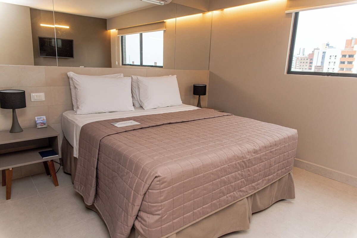Una habitación de hotel con cama, mesitas de noche, televisión y ventana con vista a la ciudad.