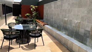 Un patio al aire libre con una mesa redonda y sillas, una fuente de agua y una jardinera con follaje.