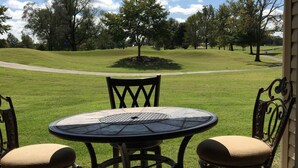 A patio with a round table and chairs, overlooking a grassy area with trees and a clear sky. - Walk in level. 3 King beds, , massage chair. Water Bubble Cascade . (Branson)