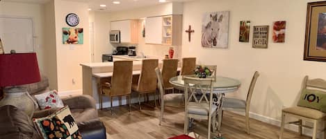 A modern living room with a brown leather couch, a glass coffee table with a red runner, and a dining area with a glass table and chairs.
