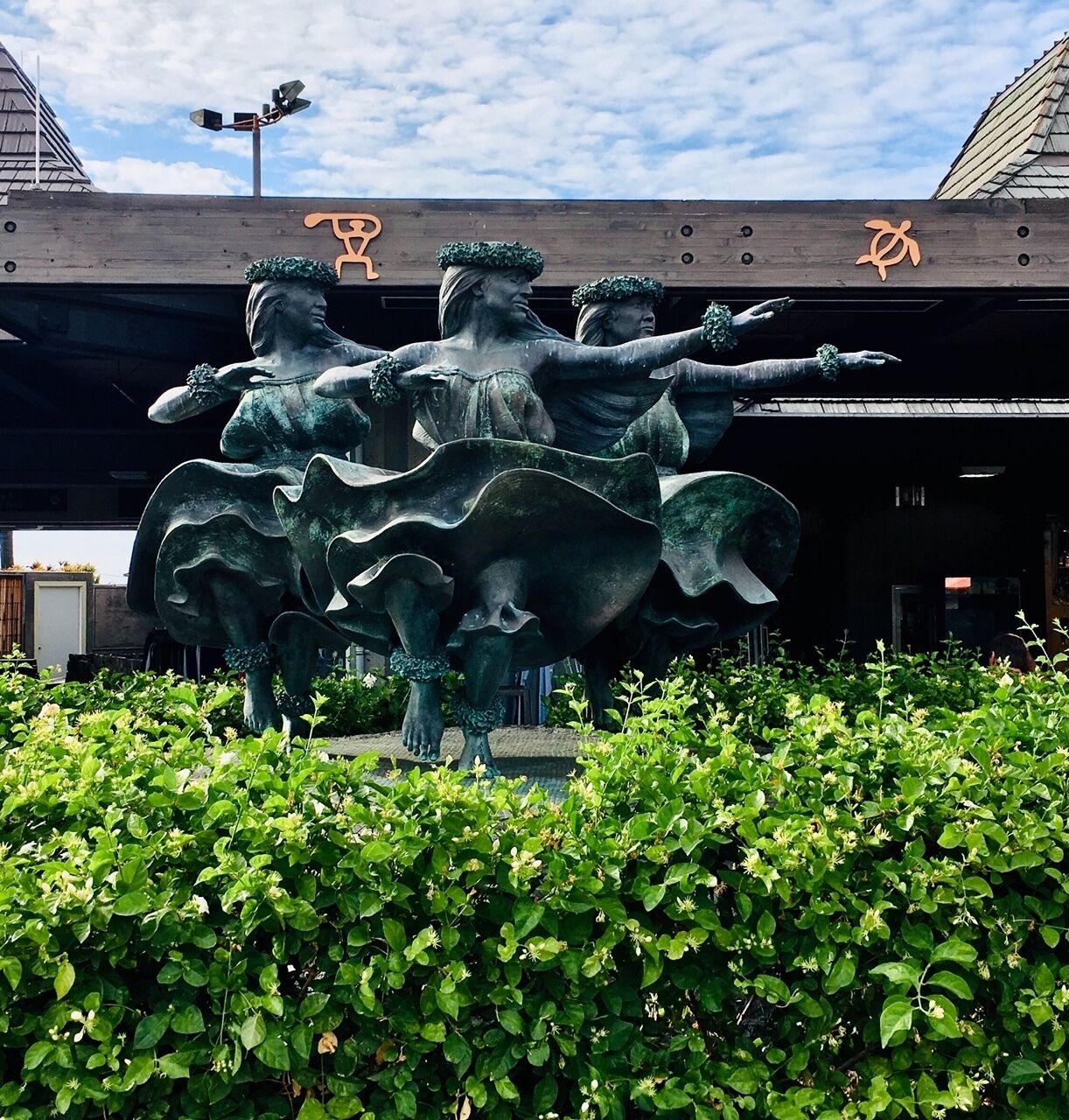 A bronze statue of three figures in a dynamic pose, set in a landscaped area with green foliage.