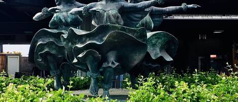 A bronze statue of three figures in a dynamic pose, set in a landscaped area with green foliage.