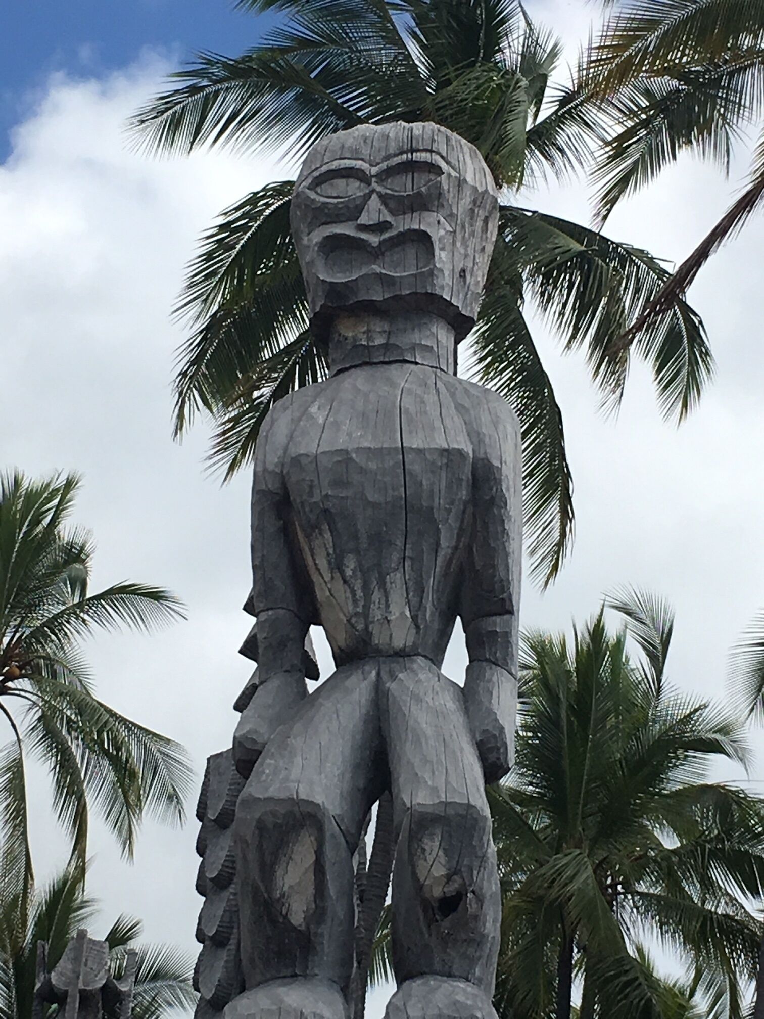 Eine große Steinstatue einer Figur mit Kopfschmuck, umgeben von Palmen.