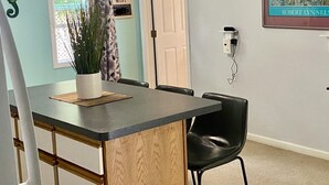 Ein Essbereich mit einem kleinen Inseltisch, schwarzen Stühlen, einer Topfpflanze und einem Deckenventilator.