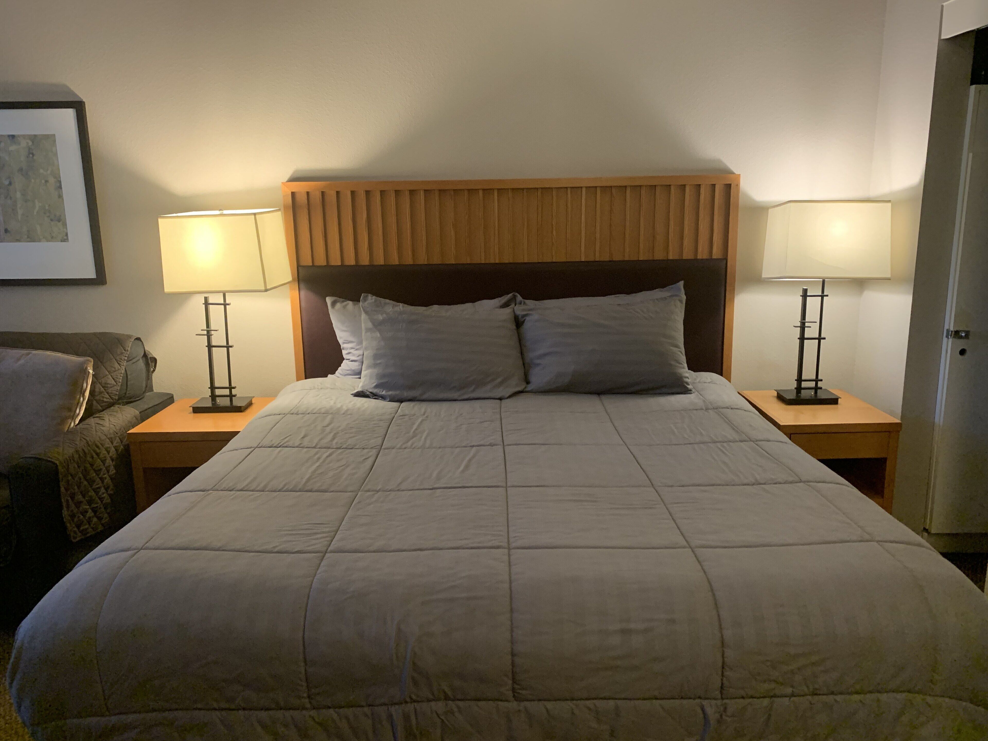 A neatly made bed with a wooden headboard, two bedside lamps, and a framed picture on the wall.
