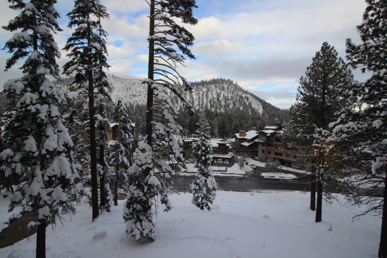 A snow-covered landscape with a mountain in the background, a river, and a building with a snow-covered roof.
