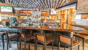 Un espace bar doté d’un long comptoir, de nombreux tabourets et d’un plafond orné de décorations sphériques suspendues.