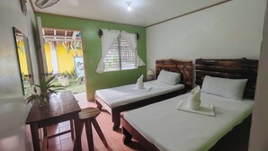 Una habitación con dos camas, una mesa, un ventilador y una ventana con cortinas.
