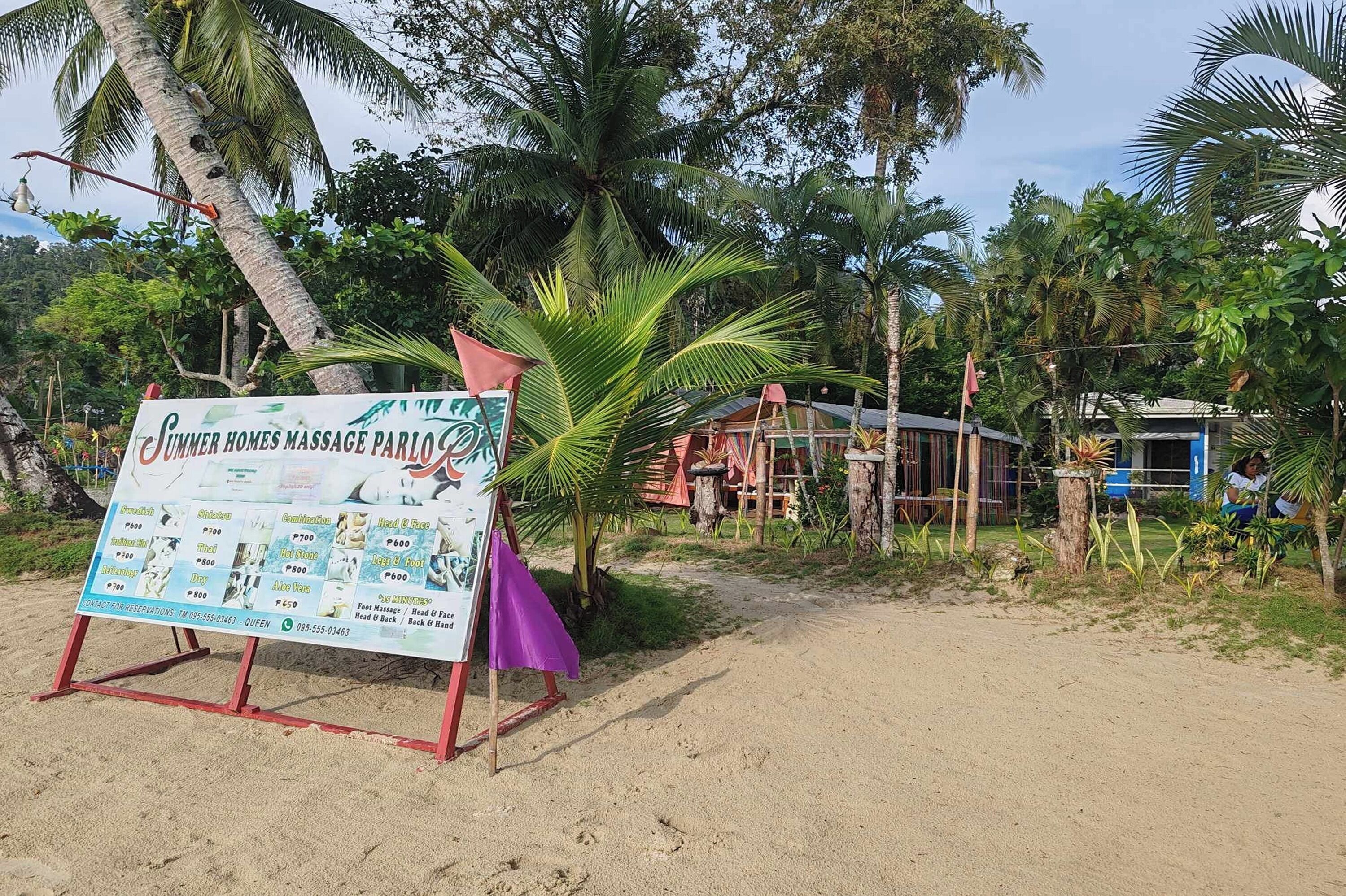 Letrero de un salón de masajes frente a la playa que enumera varios servicios.
