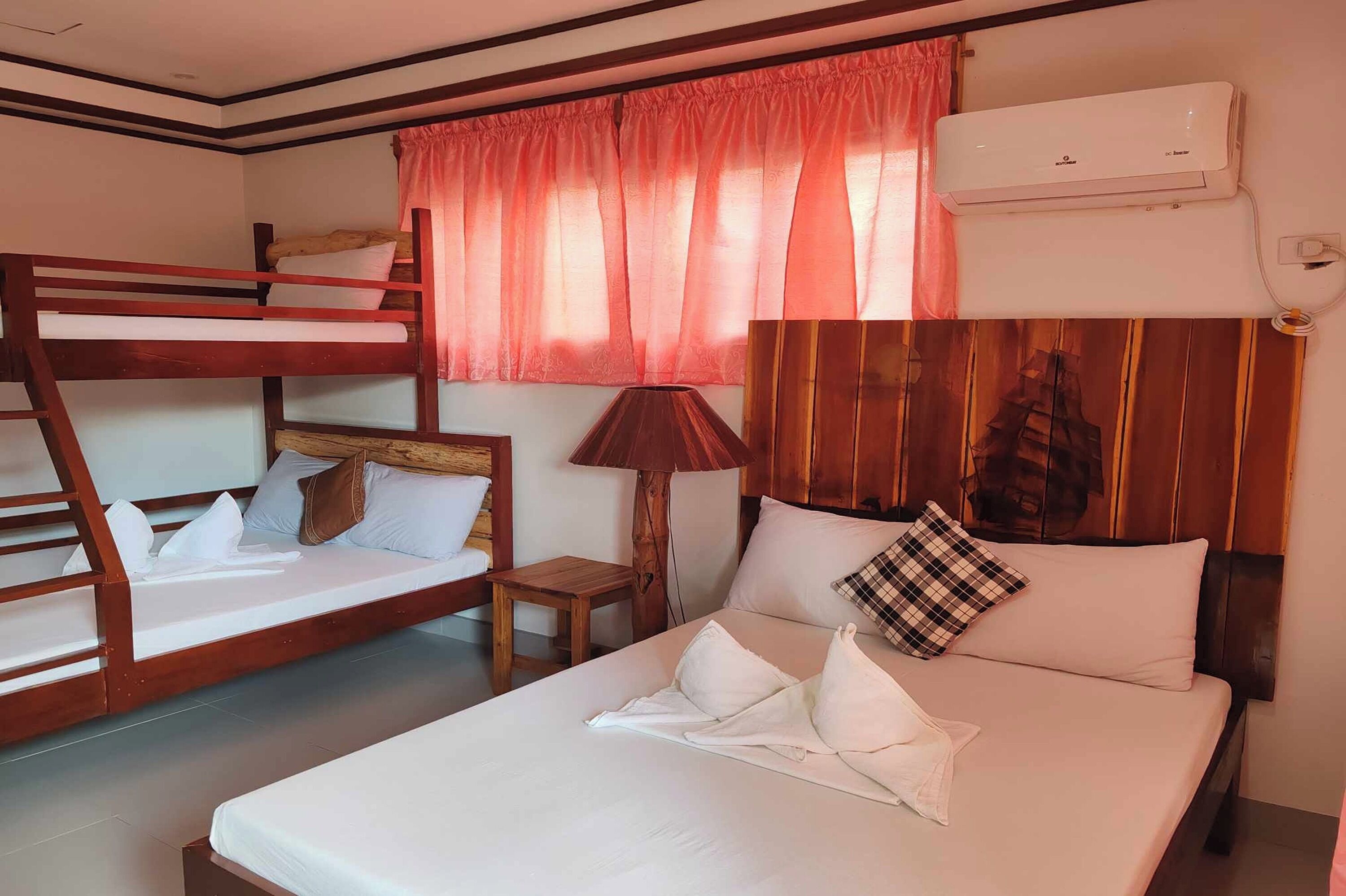 Habitación de hotel con una cama litera, una cama individual, un cabecero de madera, una lámpara y un equipo de aire acondicionado.