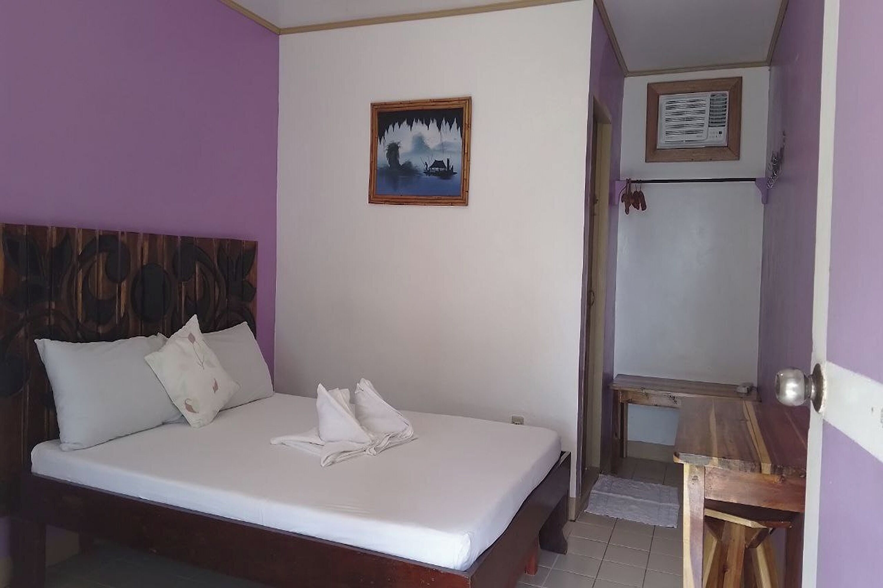Una habitación con una cama, cabecero de madera, un cuadro en la pared y una mesita.