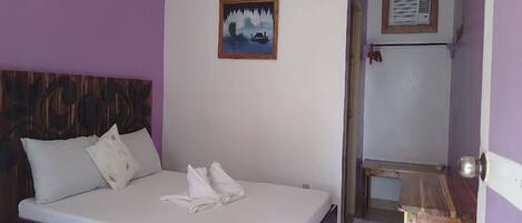 Una habitación con una cama, cabecero de madera, un cuadro en la pared y una mesita.