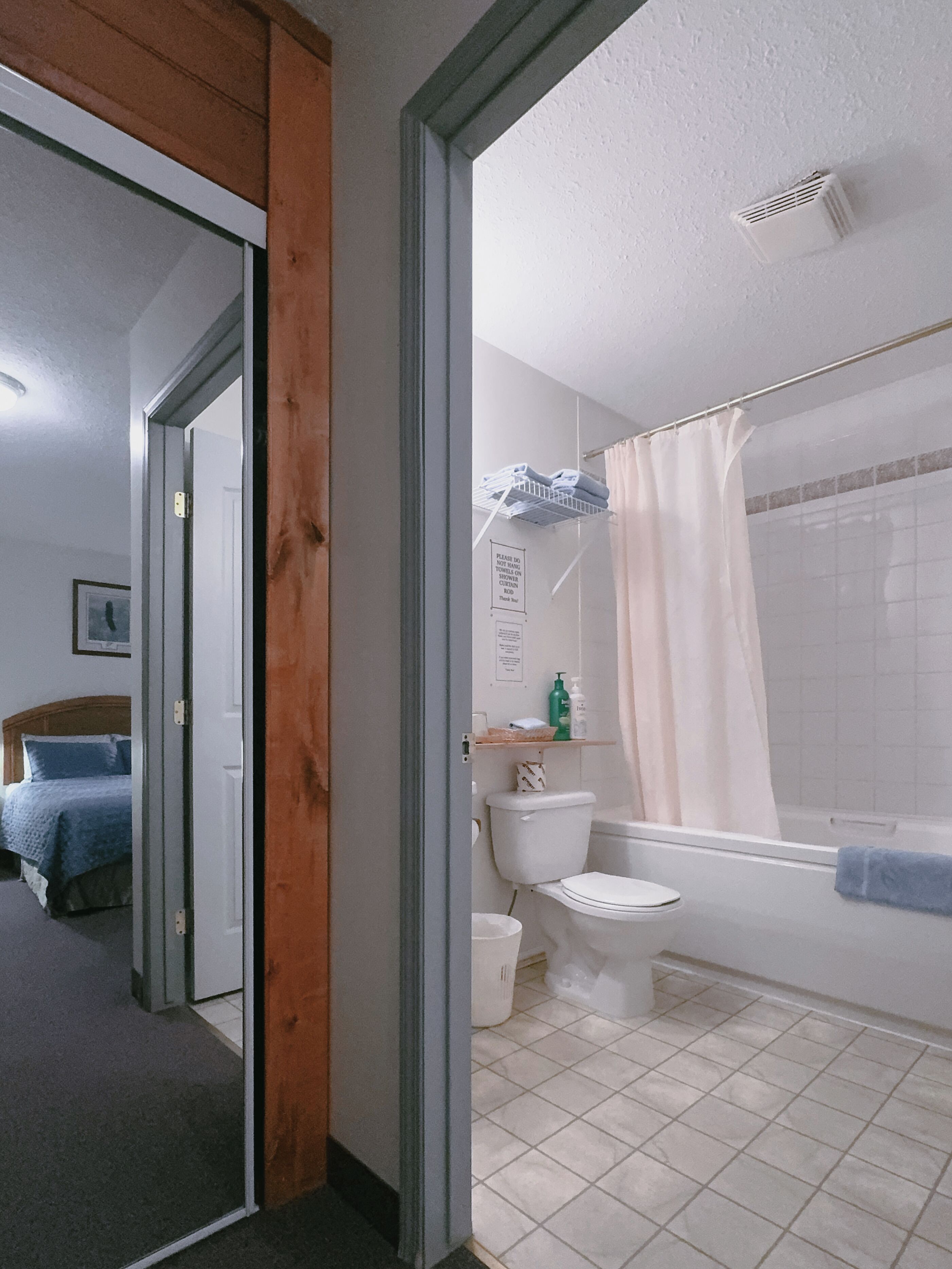 Ein Badezimmer mit Dusche und Toilette, aus dem ein Bett im angrenzenden Raum sichtbar ist.