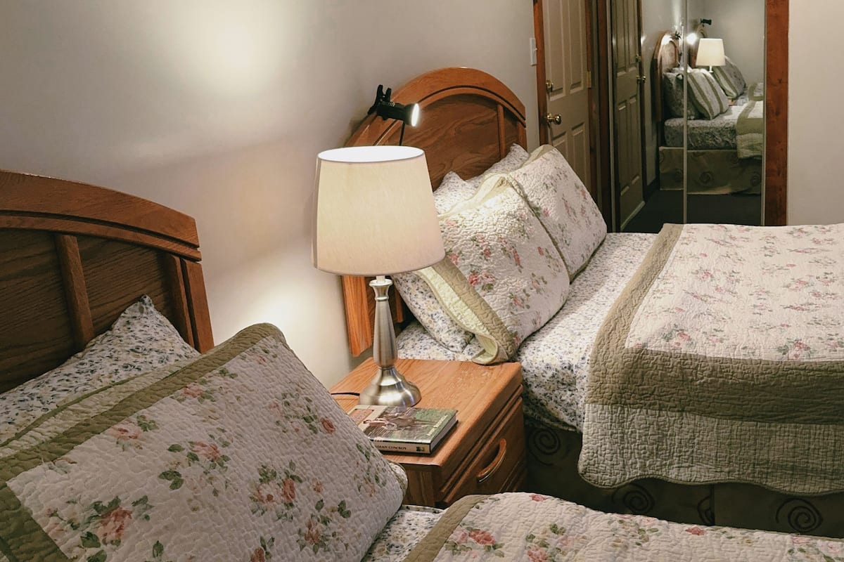 A bedroom with two beds, a nightstand, a lamp, and a wooden headboard.