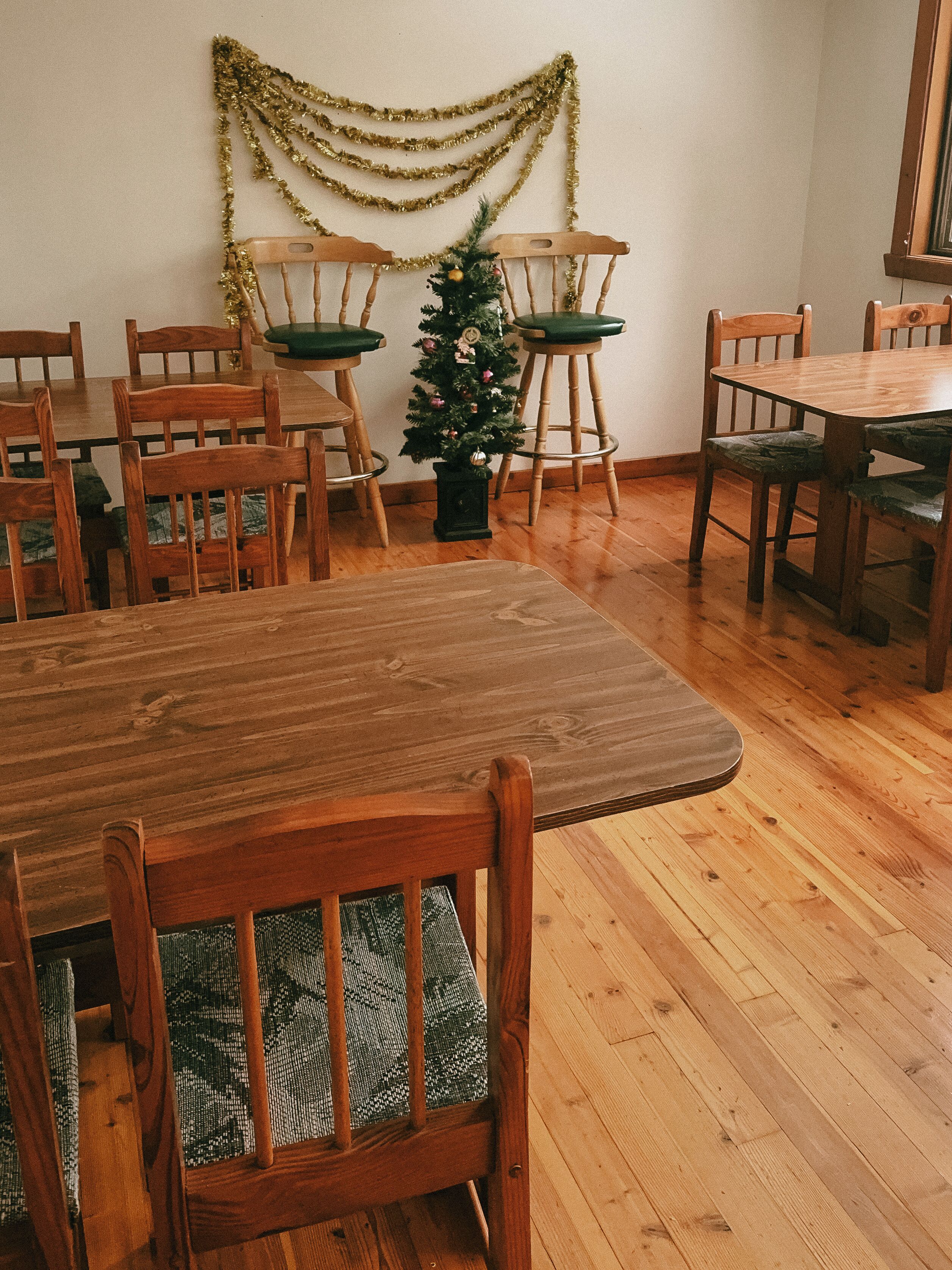 A dining area with wooden furniture, a small Christmas tree, and gold tinsel decorations.