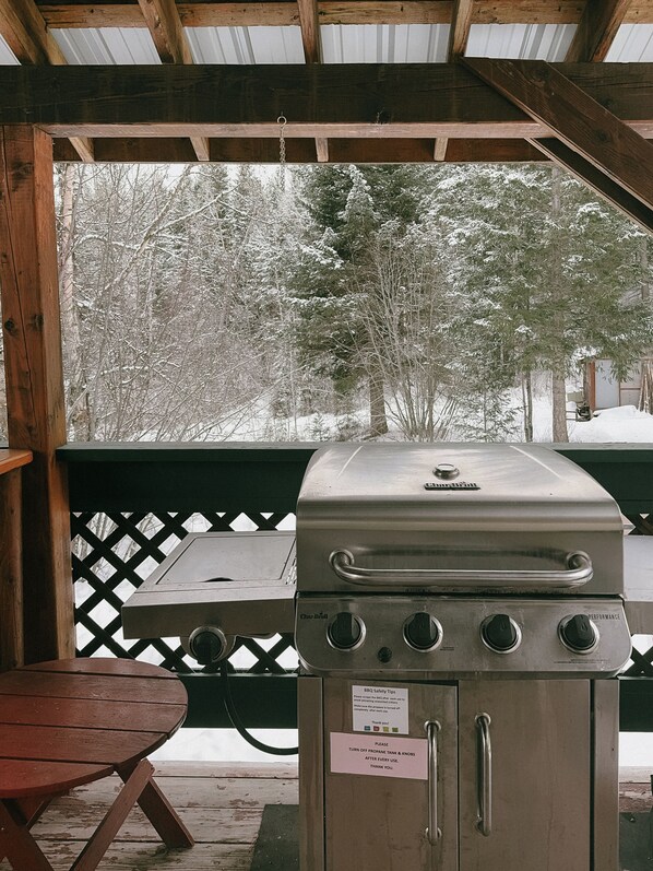 A covered outdoor grill area with a table and a view of snow-covered trees.