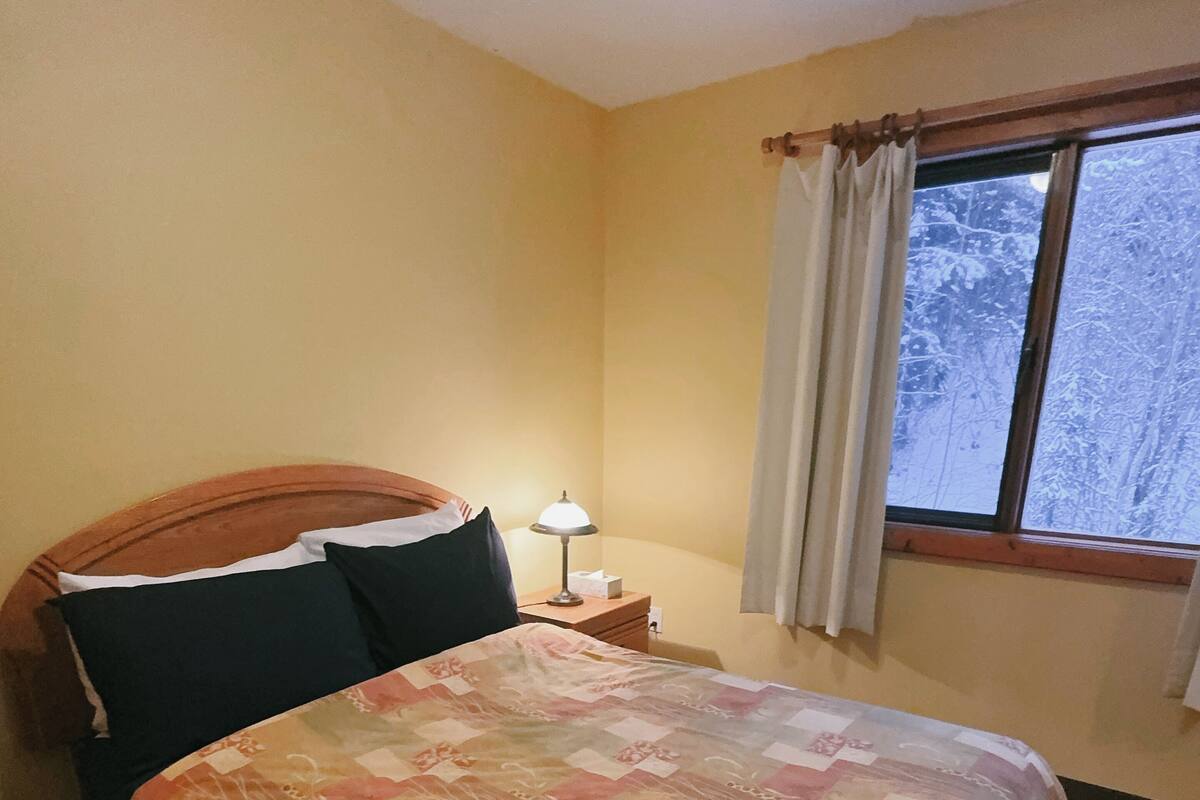 A hotel room with a bed, a nightstand, a lamp, and a window with curtains.