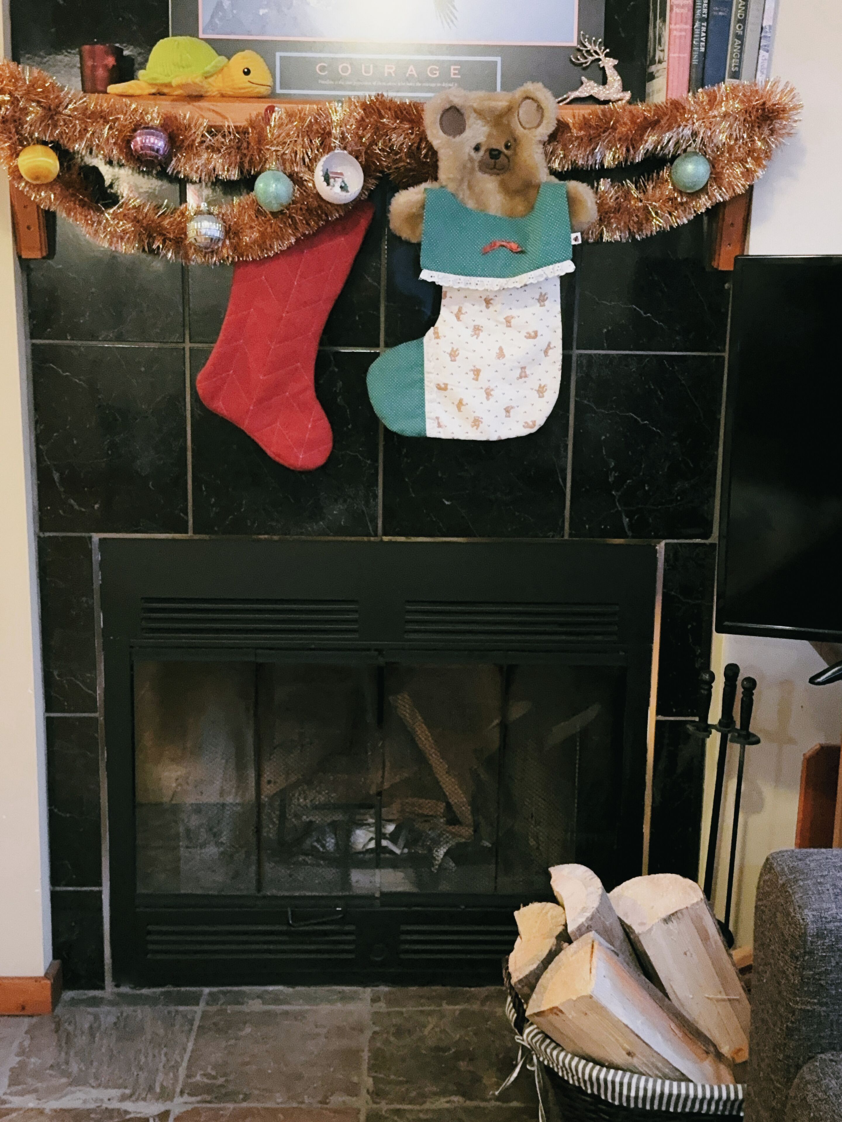 A fireplace with a bear-themed Christmas stocking and a garland above it.