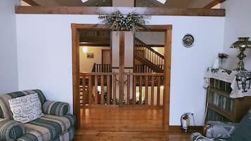 A spacious living room with wooden floors and a high ceiling. There is a staircase leading to an upper level, and a wooden railing separates the two floors.