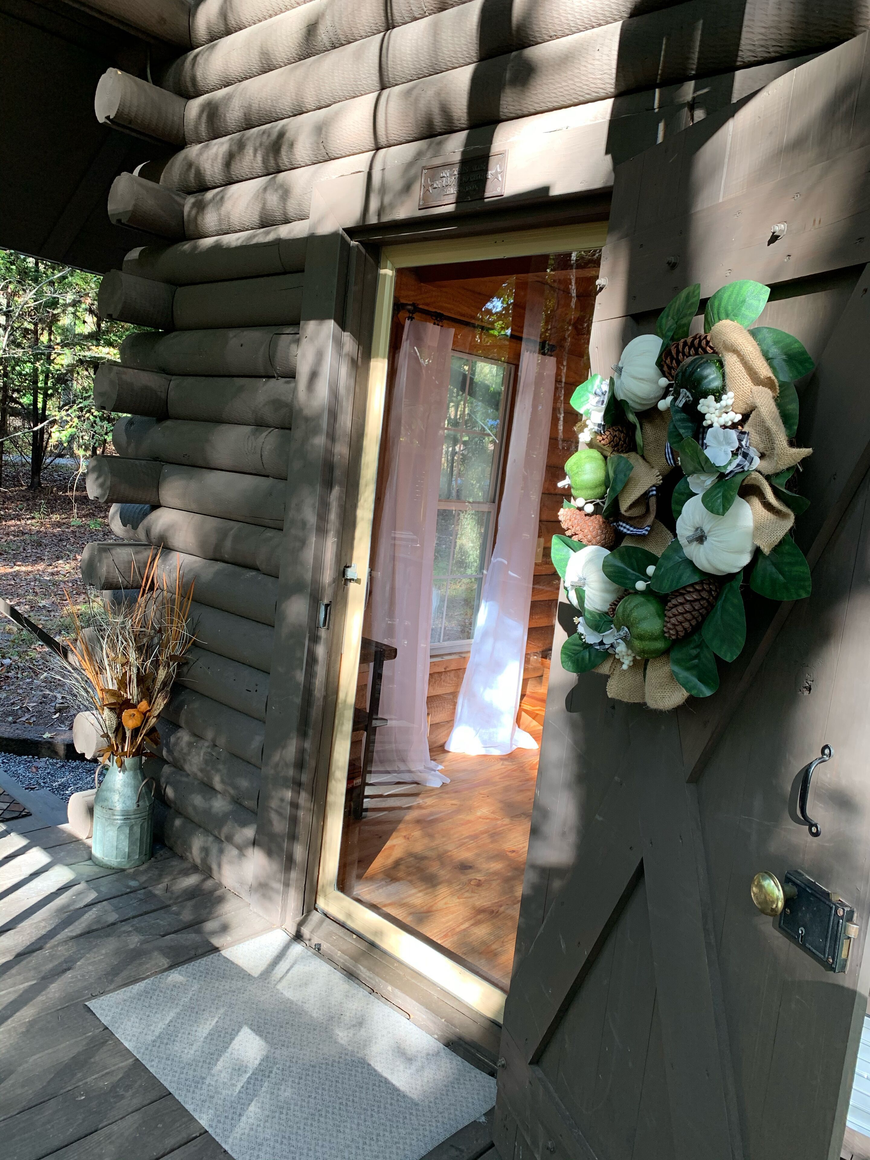 A wooden cabin entrance with a door, a decorative wreath, and a vase with dried plants.