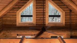 A cabin with a wooden interior, two windows with black frames, and a ceiling fan.
