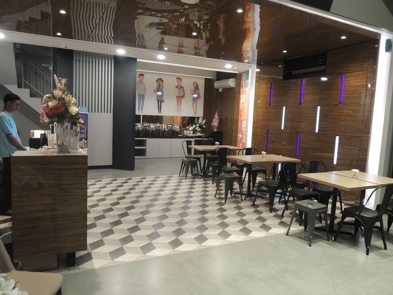 A modern restaurant interior with a checkered floor, wooden tables, black chairs, and a central counter with a floral arrangement.