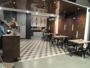 Interior moderno de restaurante con piso a cuadros, mesas de madera, sillas negras y una barra central con un arreglo floral.