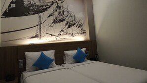 A hotel room with a large black and white mural on the wall, a wooden headboard, and two beds with blue pillows. - Odua Thamrin Jakarta (Jakarta)
