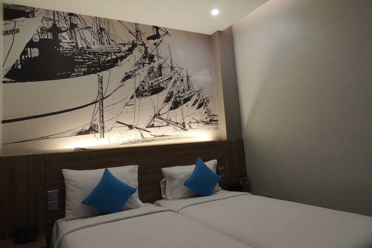 Habitació d'hotel amb un mural gran en blanc i negre a la paret, un capçal de llit de fusta i dos llits amb almoades blaves.