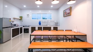A modern kitchen with a dining area, featuring a large wooden table, pendant lights, and a window with a city view. - Baan Farm Sook (Cha-am)