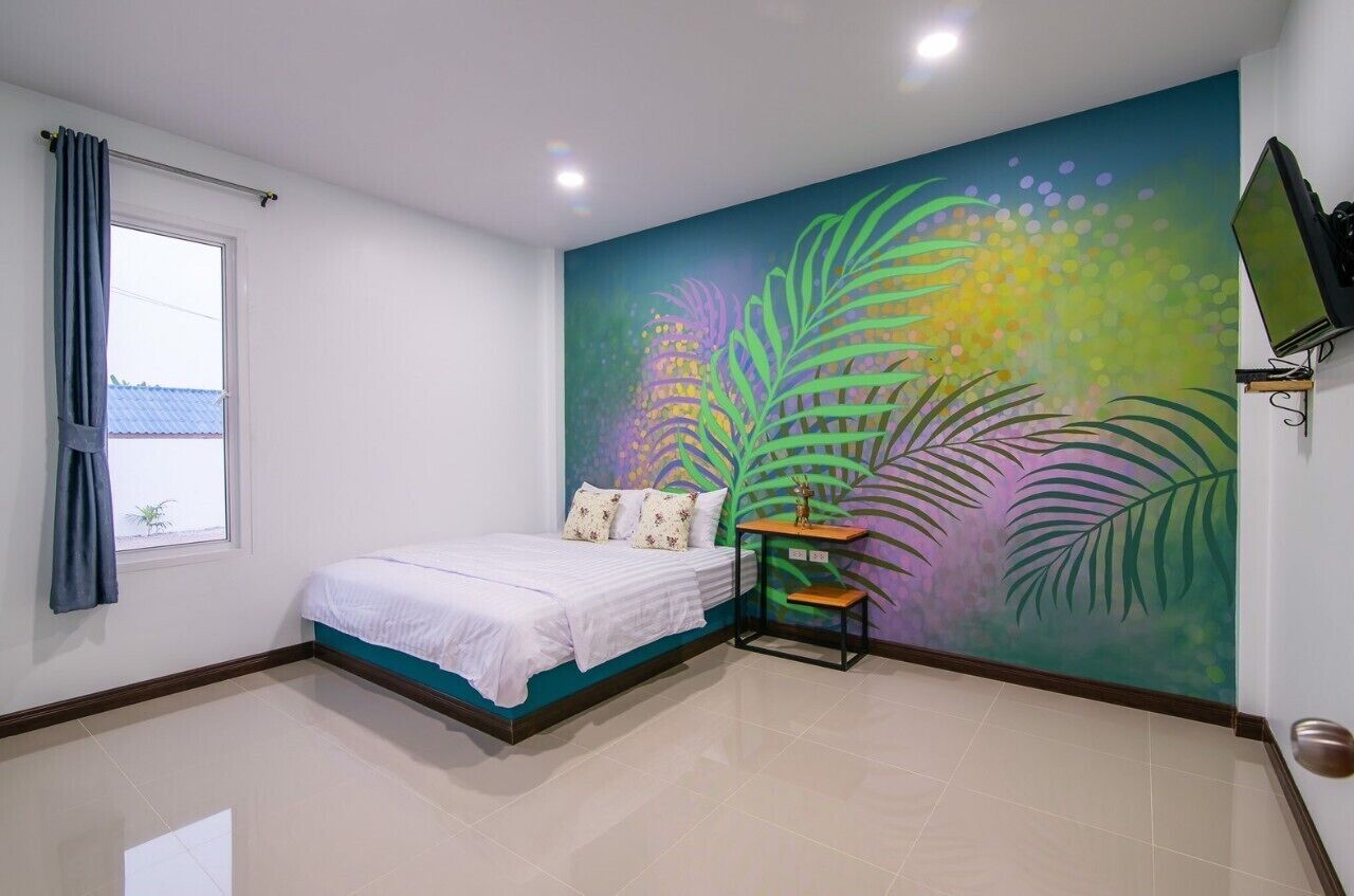 Un dormitorio con cama, ventana con cortinas, televisión montada en la pared y un mural colorido.