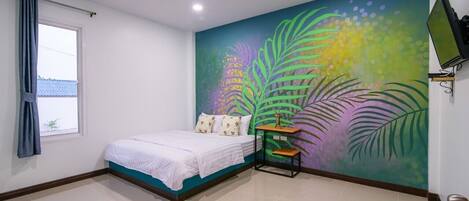 Un dormitorio con cama, ventana con cortinas, televisión montada en la pared y un mural colorido.