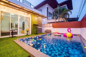 Una casa moderna con piscina, un patio con mesa y sillas, y un balcón con vistas al cielo.