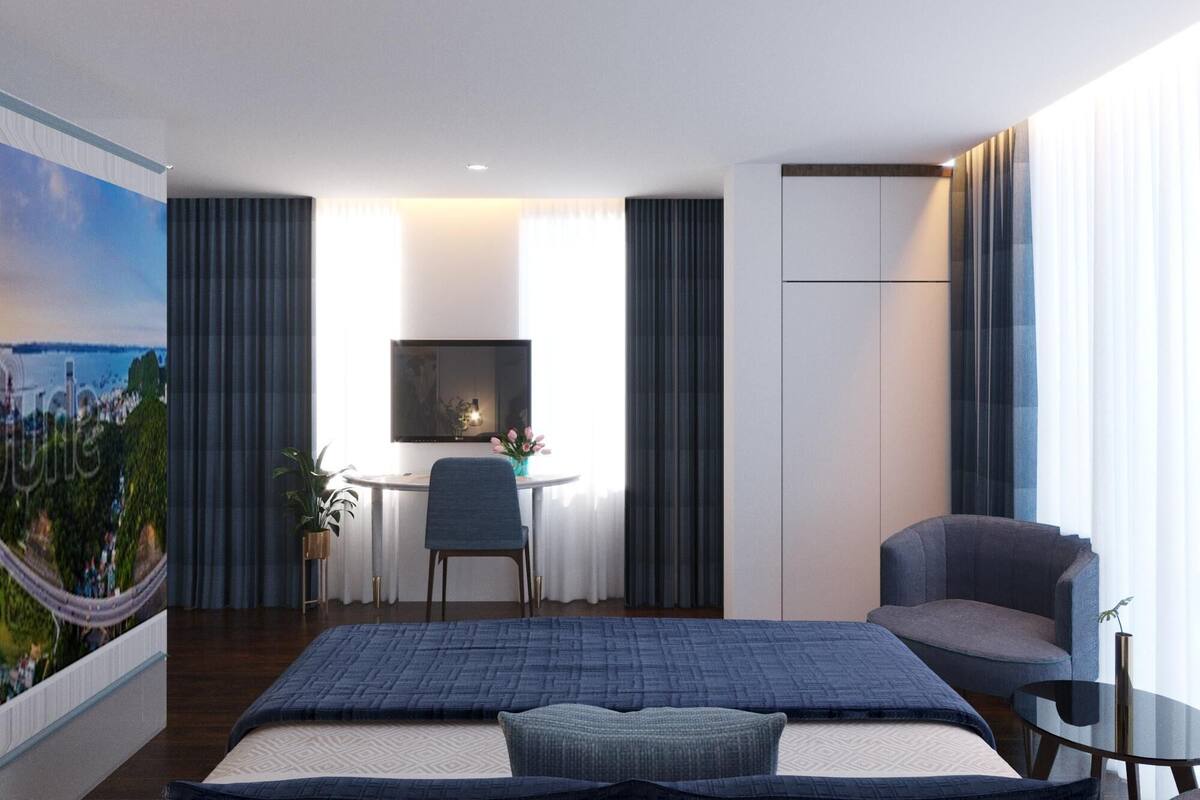 Une chambre d’hôtel moderne avec un grand lit, un bureau et une chaise. Il y a un téléviseur accroché au mur et une fenêtre avec des rideaux.