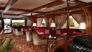 A luxurious interior with a red sofa set, leather armchairs, and a dining table with lamps. - Jaz Monarch Nile Cruise - Every Monday from Luxor for 07 and 04 Nights - Every Friday From Aswan for 03 Nights (Luxor)