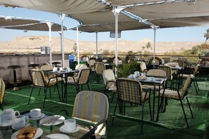 Un espace extérieur aménagé pour les repas, avec des tables et des chaises, offrant une vue sur le désert en arri ère-plan, ainsi qu’un espace de repos abrité.