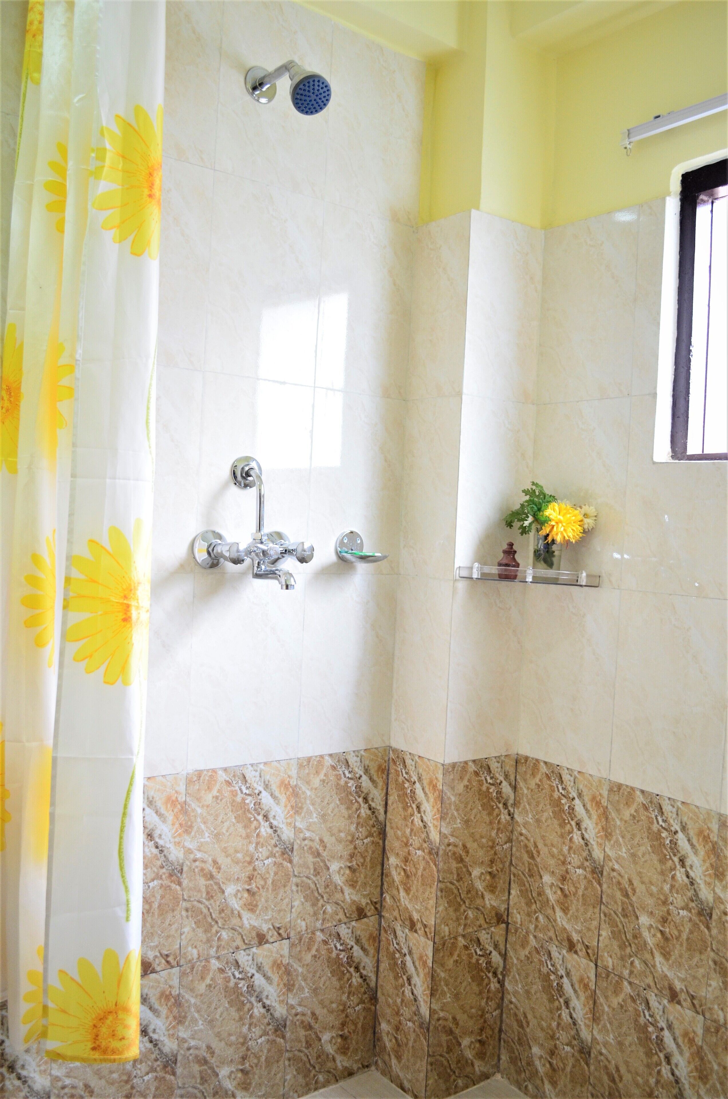 Un baño con ducha, espejo y repisa con una flor.