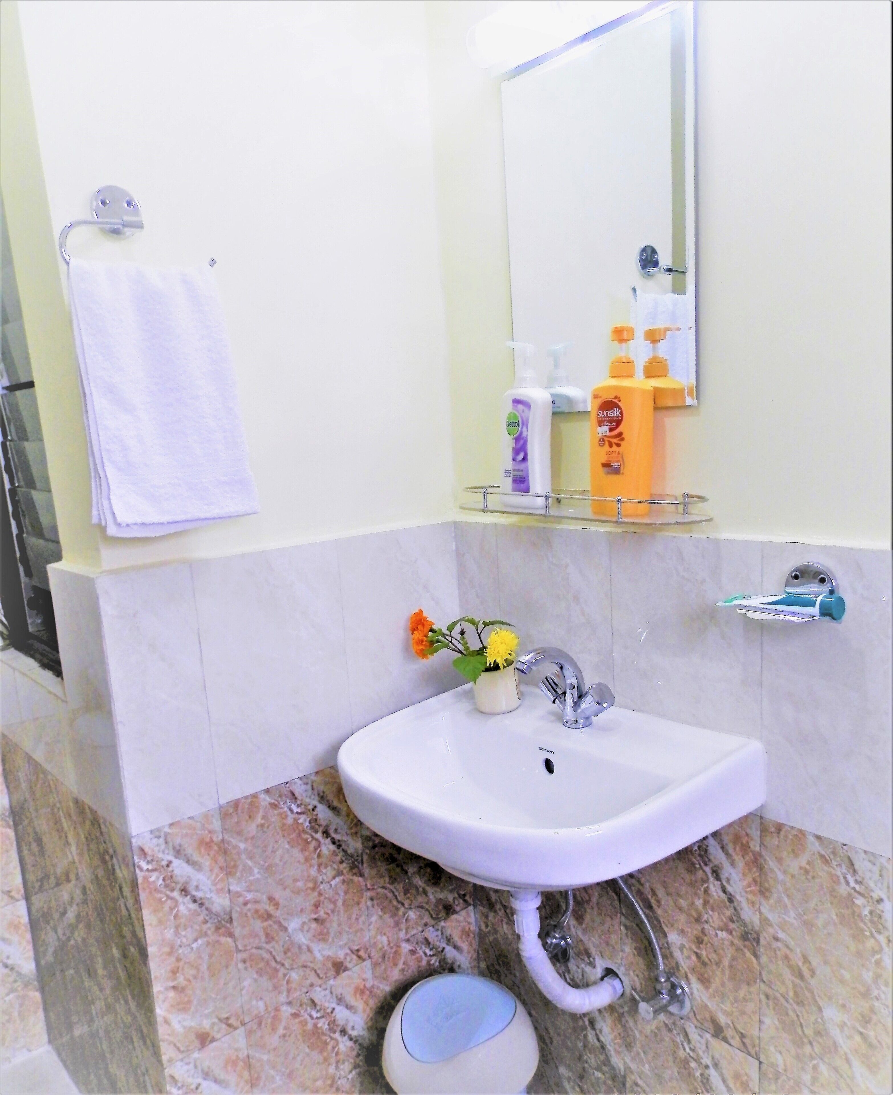 Un baño con un lavamanos blanco, un espejo, un perchero para toallas y artículos de tocador en un estante.