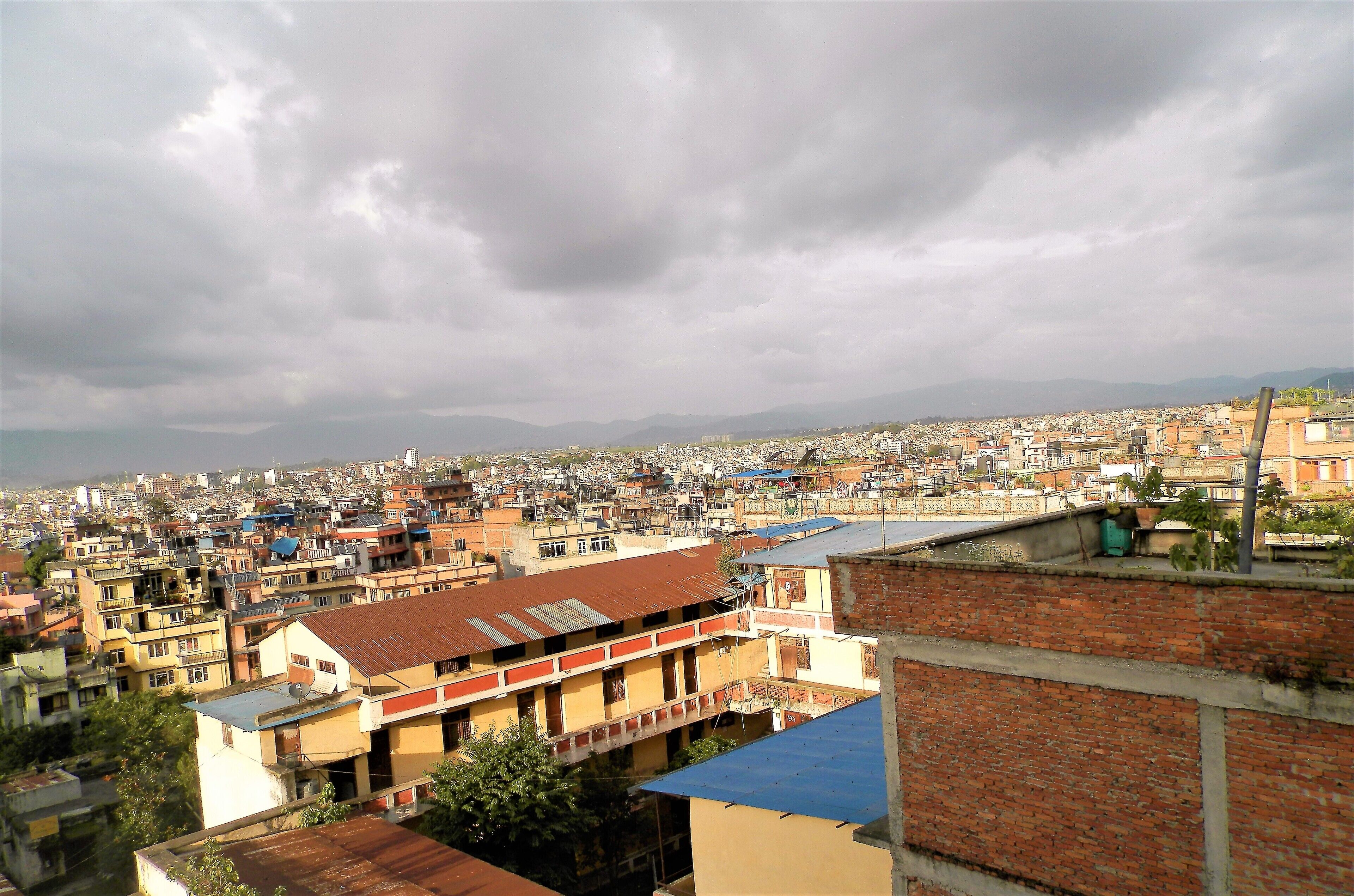 Área urbana densamente poblada con numerosos edificios y una cadena montañosa distante bajo un cielo nublado.
