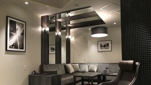 A modern living room with a sectional sofa, a leather armchair, a coffee table, and a dining table. There are framed pictures on the walls, a large mirror, and a textured wall panel. - Hotel Gaudium - Adult Only (Kuki)