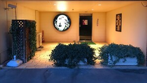 A hotel entrance with a circular wall decoration, a door, and a small garden area. - Hotel Gaudium - Adult Only (Kuki)