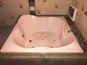 A large, freestanding bathtub with a control panel, set against a tiled wall with floral patterns.