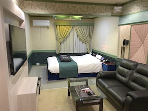 A hotel room with a bed, a leather sofa, a glass coffee table, a TV, and a telephone.