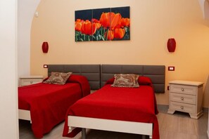 A bedroom with two beds, a grey headboard, red bedding, and a wall-mounted painting of red tulips.