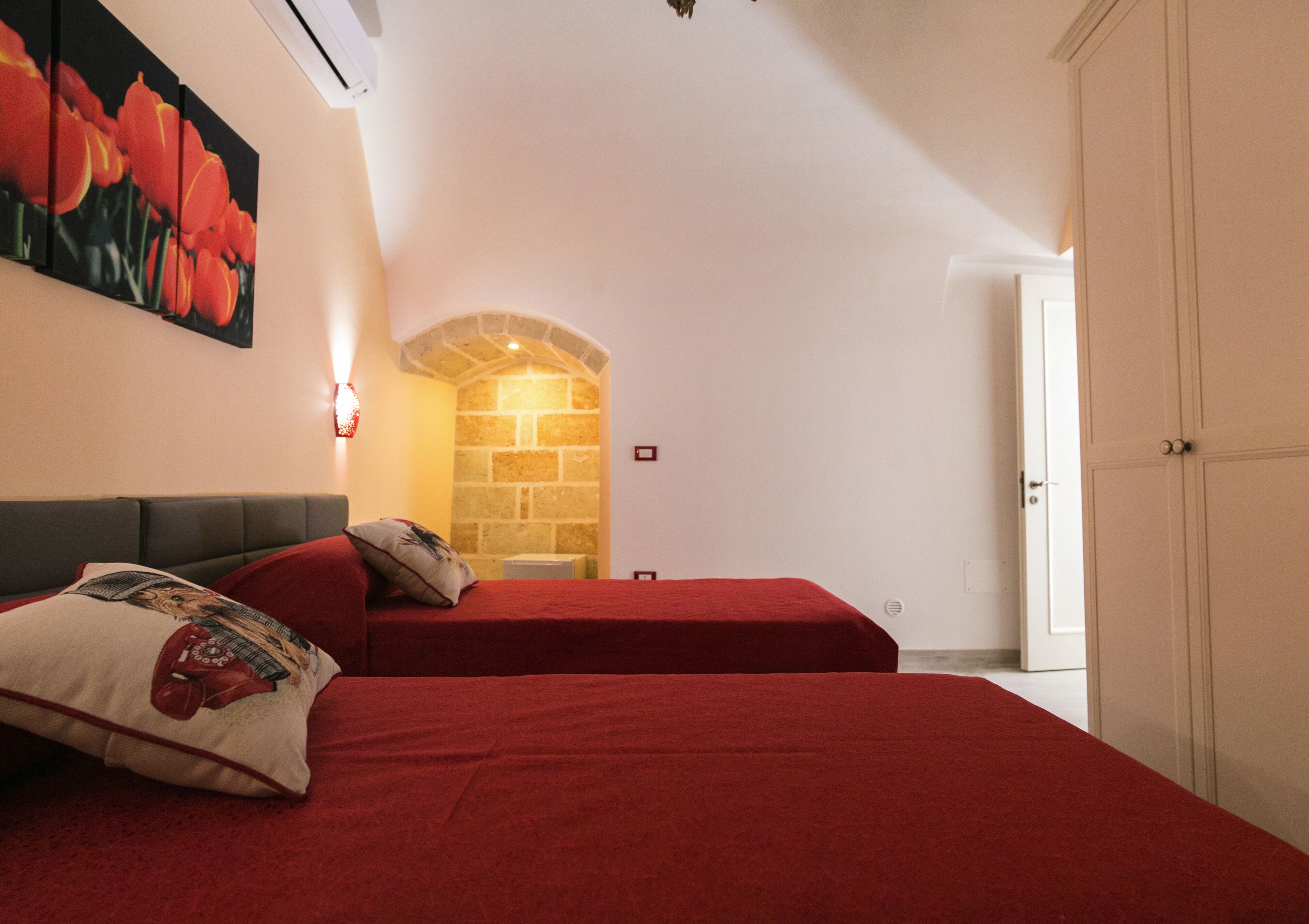 A bedroom with two beds, a stone wall, and a door leading to another room.