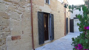 A narrow stone-paved alleyway with a building featuring a door with a diamond-patterned grille. - Casa a Corte (Copertino)