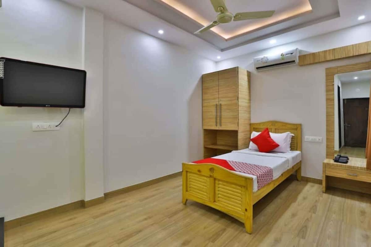 A bedroom with a bed, a TV mounted on the wall, a wardrobe, and a ceiling fan.