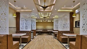 A restaurant with booths and tables, a ceiling fan, and decorative wall panels. - Hotel Centre Point (Mundra)
