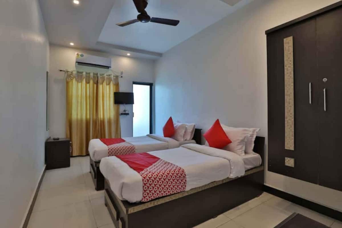 A hotel room with two beds, a ceiling fan, an air conditioning unit, a wardrobe, and a window with curtains.