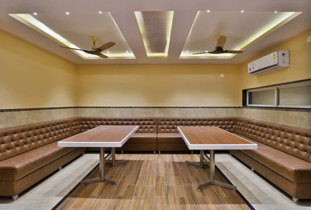 Une pièce avec un banc en cuir marron, deux tables, des ventilateurs de plafond, un éclairage encastré et un appareil de climatisation.